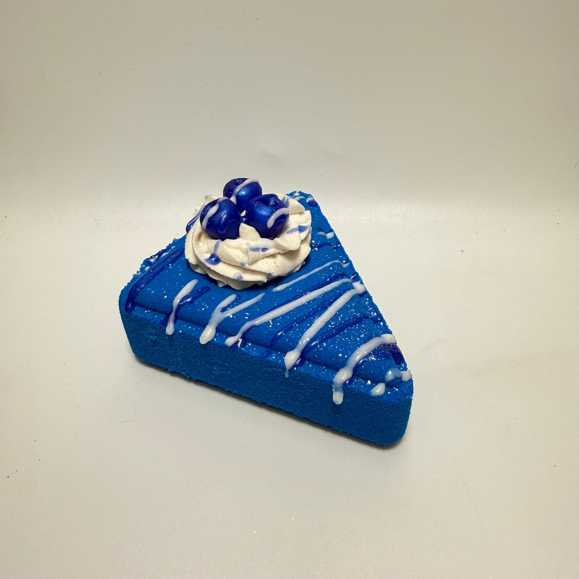 Blueberry colored pie slice bath bomb with white bubble bath frosting piped on top. Blueberry soap embedded in the frosting.