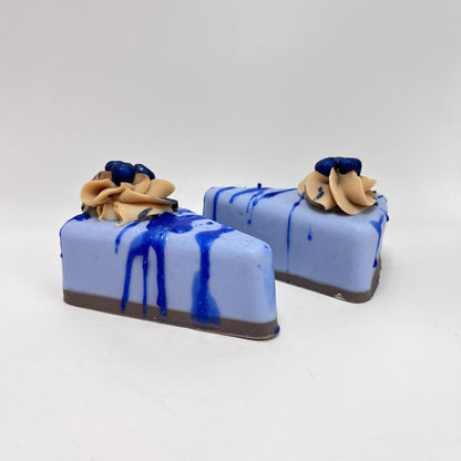 Two slices of light blue pie shaped soap. Topped with a puff of cream colored cold process soap and blueberry soaps.