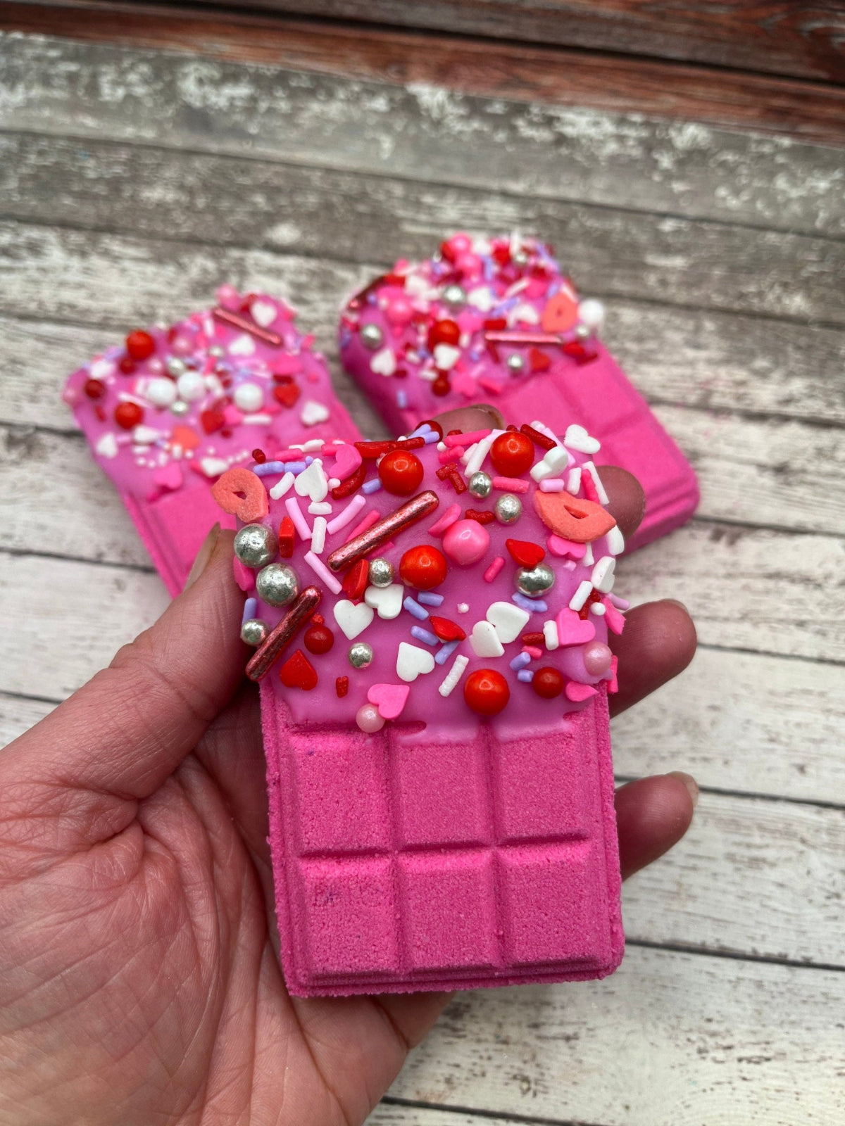 Pink candy bar bath bomb in a hand. Dipped in pink colored cocoa butter and covered in Valentine's Day themed sprinkles.