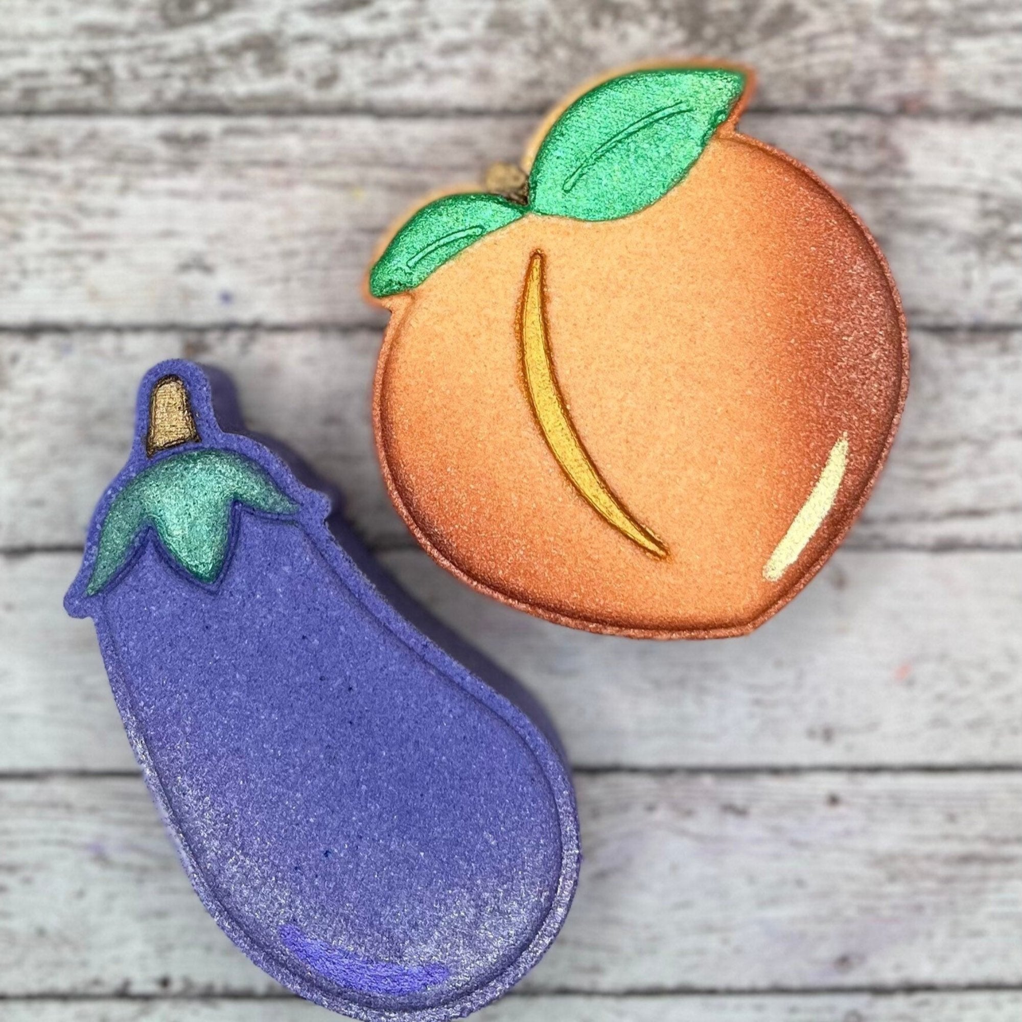 One purple eggplant shaped bath bomb and one peach colored and shaped bath bombs. 