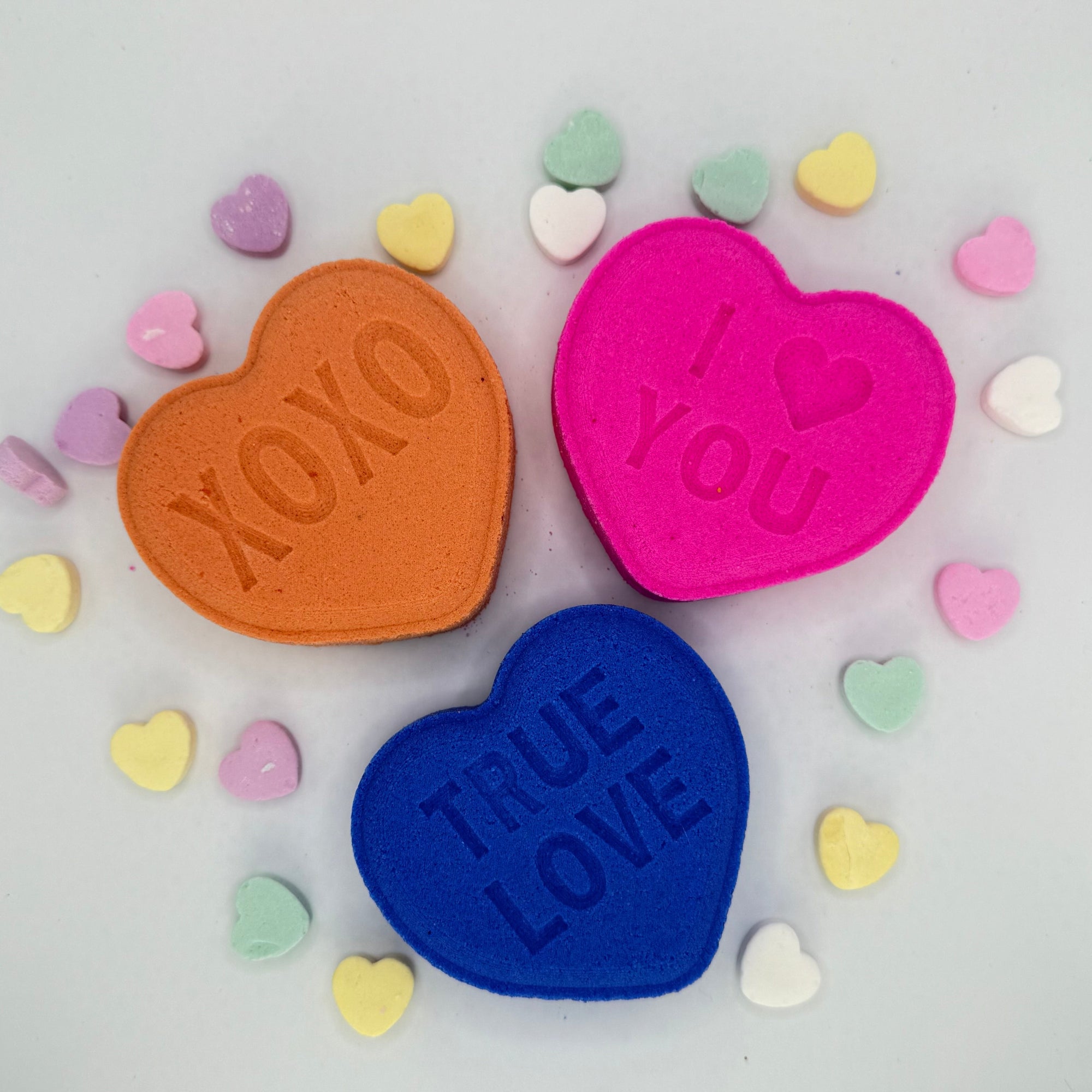 Heart bath bombs with messages from Rusted Acre Soap Company. Three hearts in pink, purple and peach.