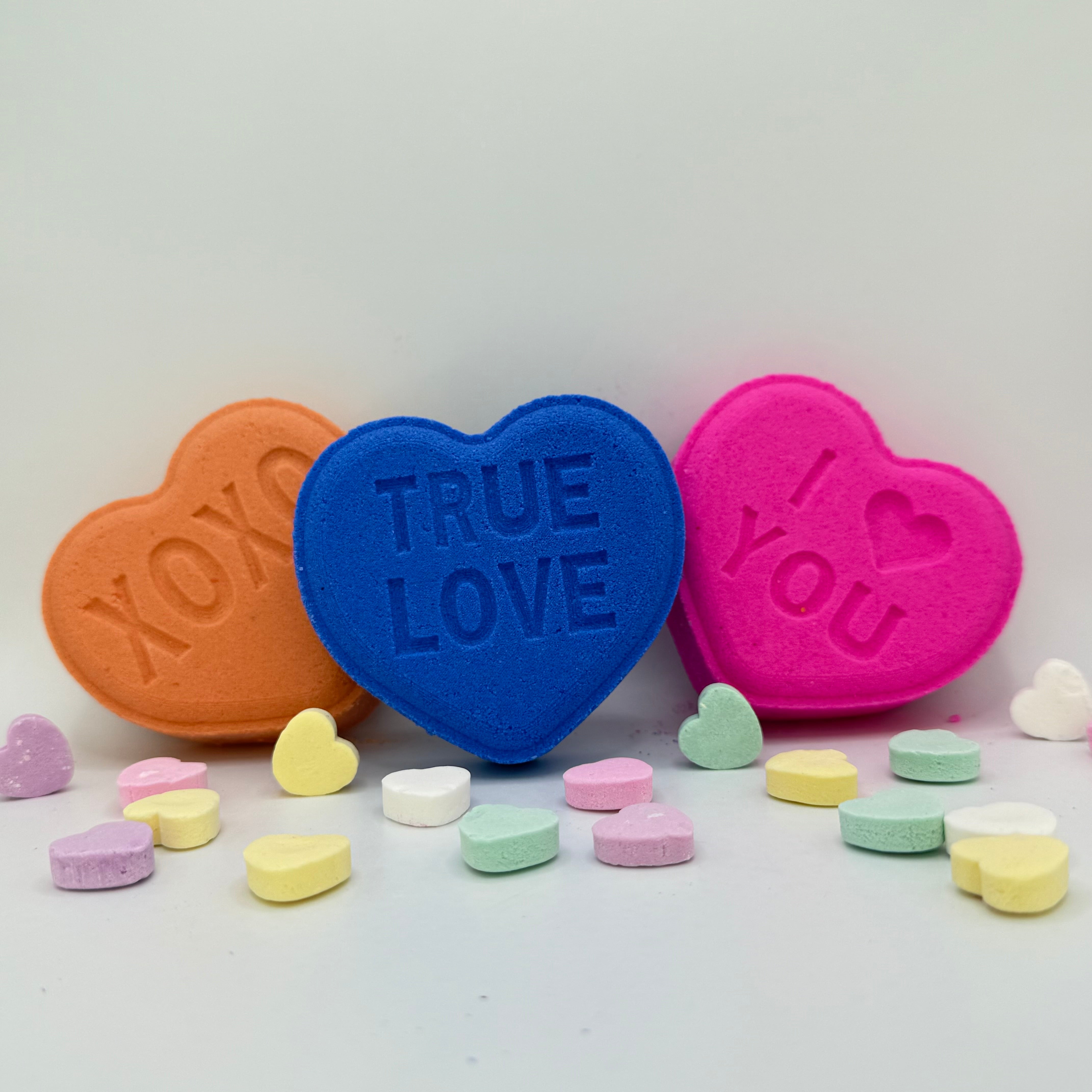 Heart bath bombs front view with messages from Rusted Acre Soap Company. Three hearts in pink, purple and peach.