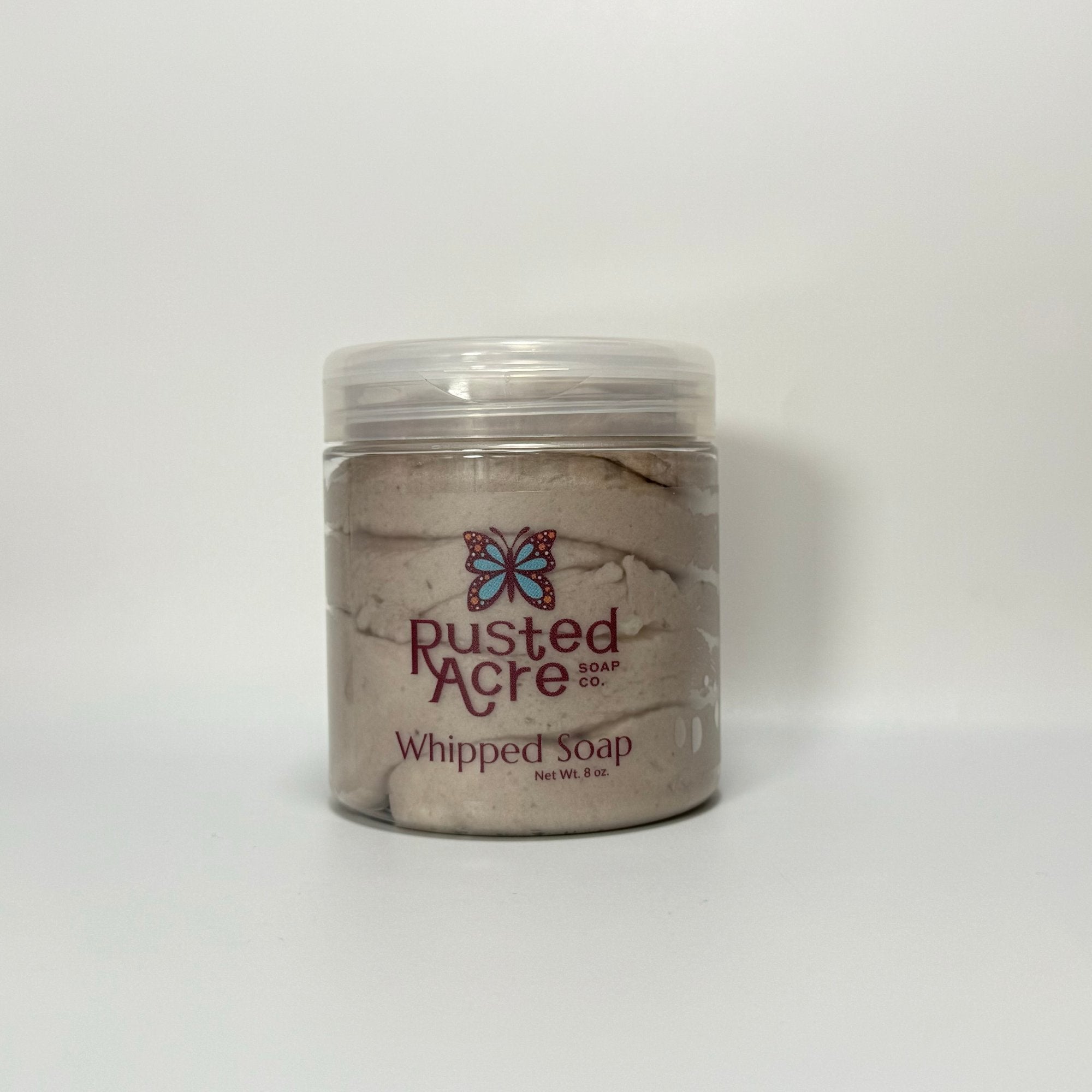 A jar of Cowboy Whipped Soap with a label reading Rusted Acre Soap Co. Whipped Soap.  It's in a clear jar and the color is light leather brown. 