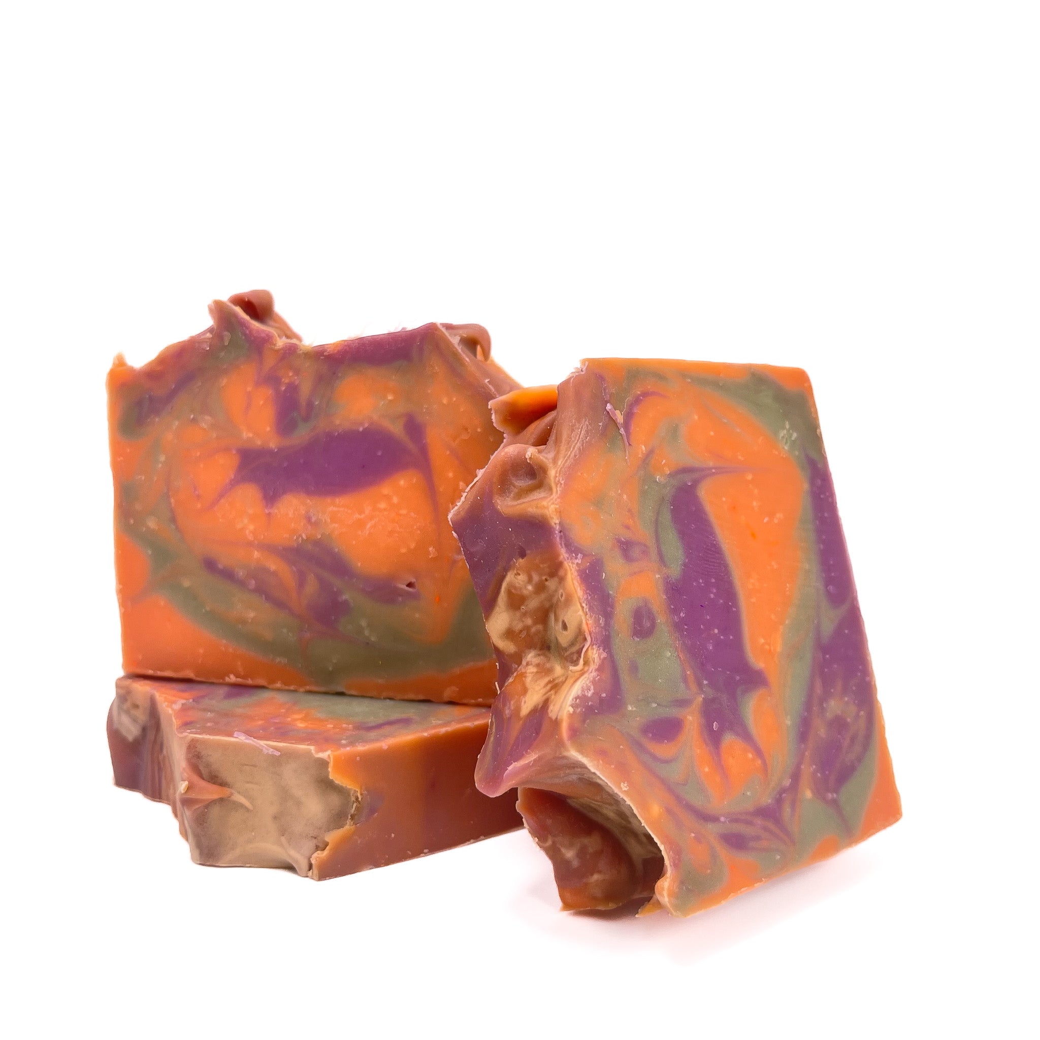 Three bars of Rusted Acre Soaps fruity cereal handmade soap. Colors are swirled bright orange, purple, and green. Top is artisan style.