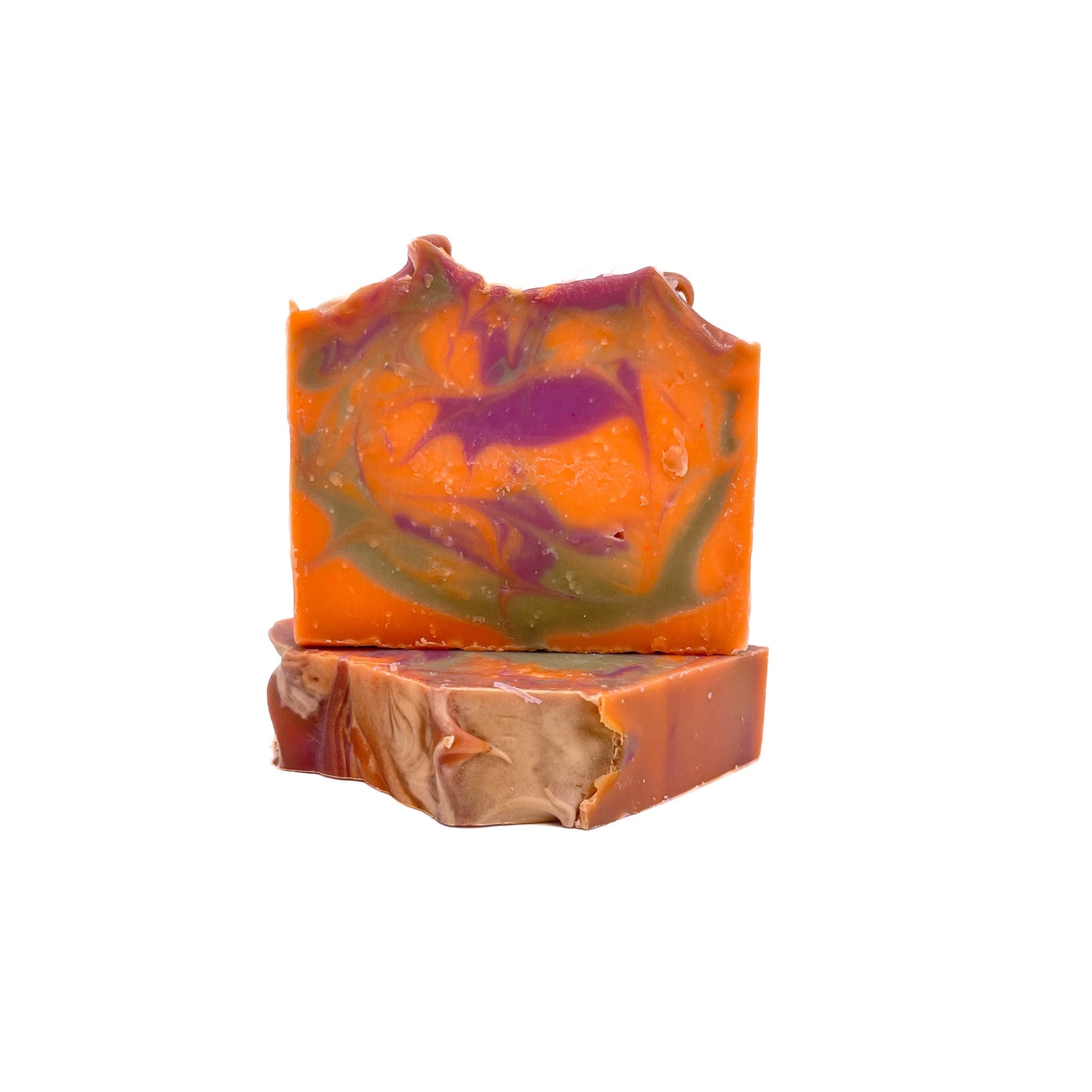 Two bars of fruity cereal handmade soap from Rusted Acre Soap Co. One lying flat one upright. The colors are bright orange, purple and green swirled together. 