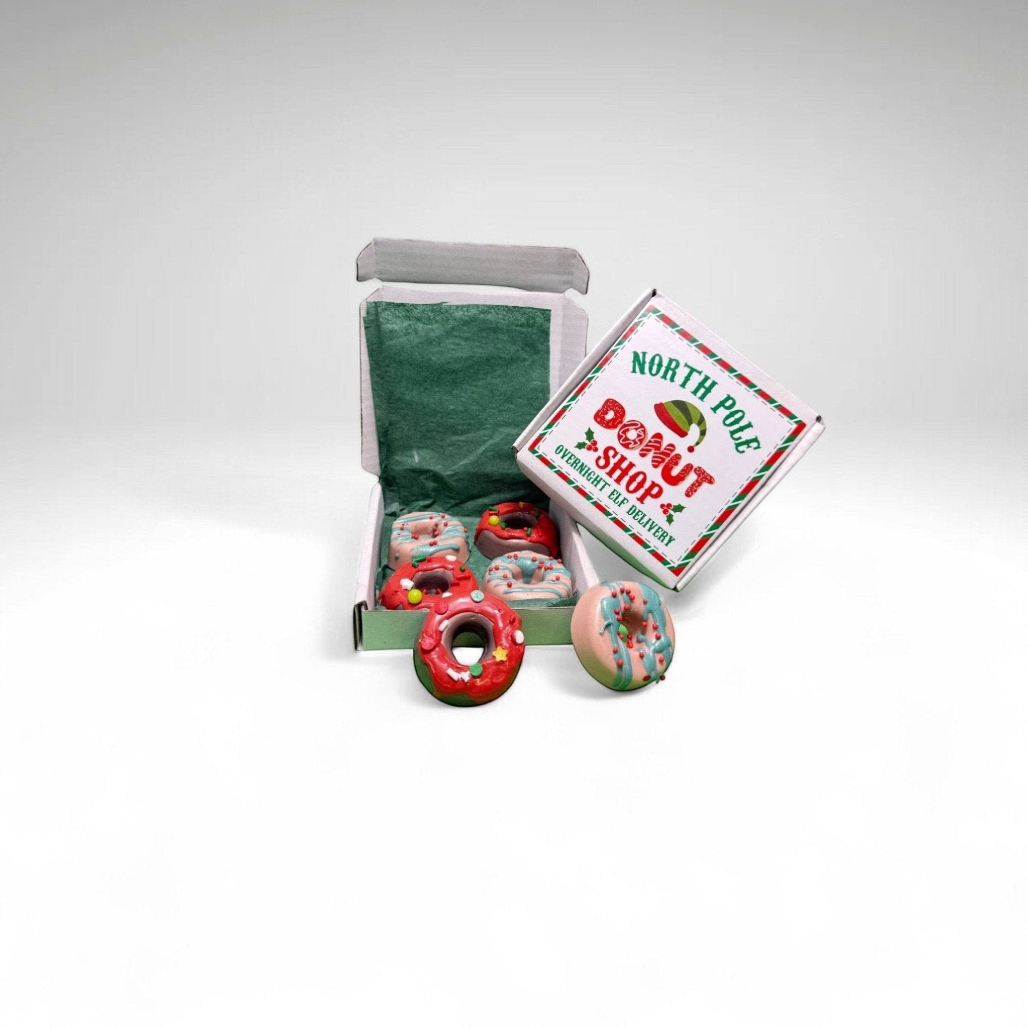 A box of mini holiday donut soaps from Rusted Acre Soap Co. Soaps are brown and tan with red or green drizzle. Box labeled North Pole Donut Shop.