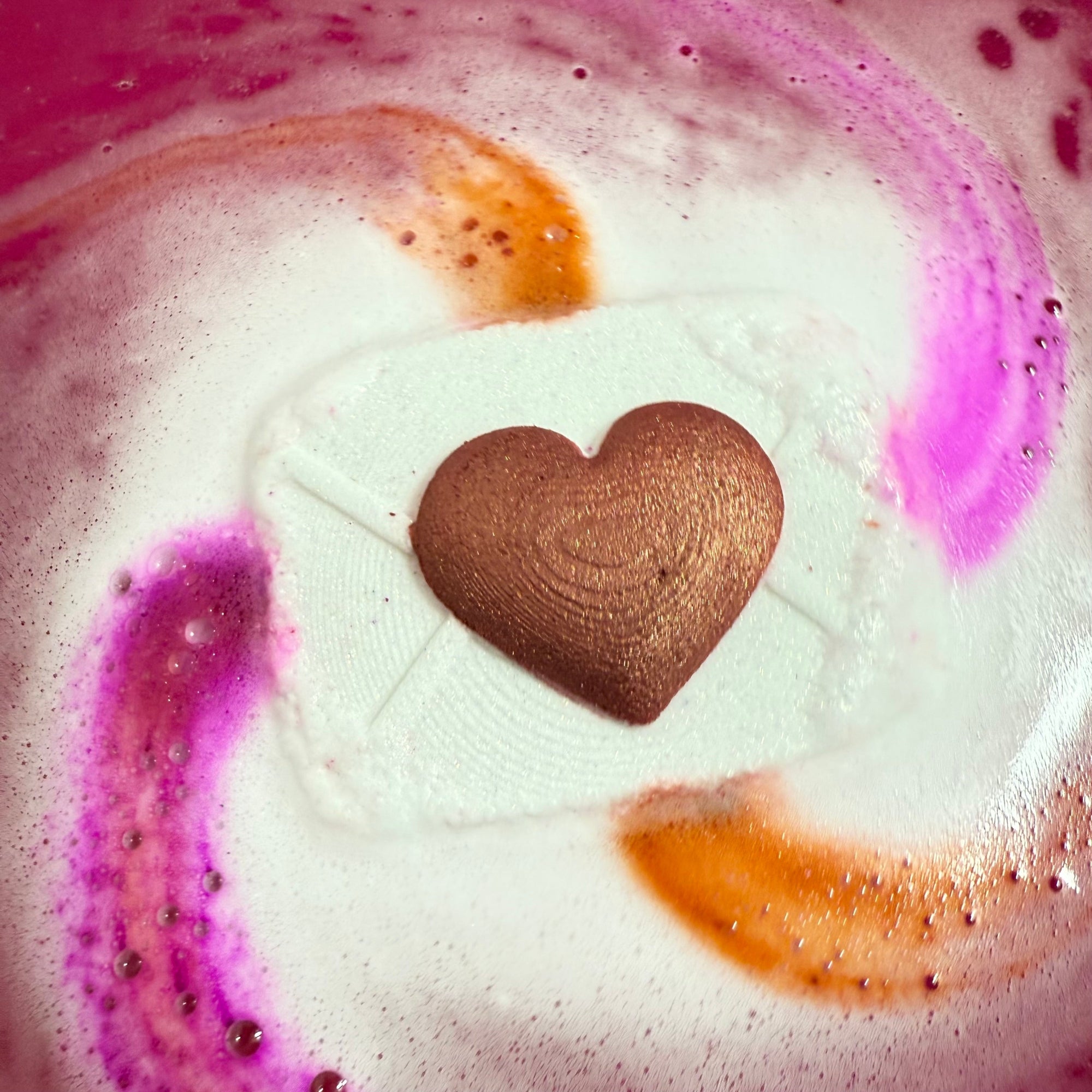 Rusted Acre Soap Co's love letter bath bomb in the water with vibrant shades of pink and red fizz.