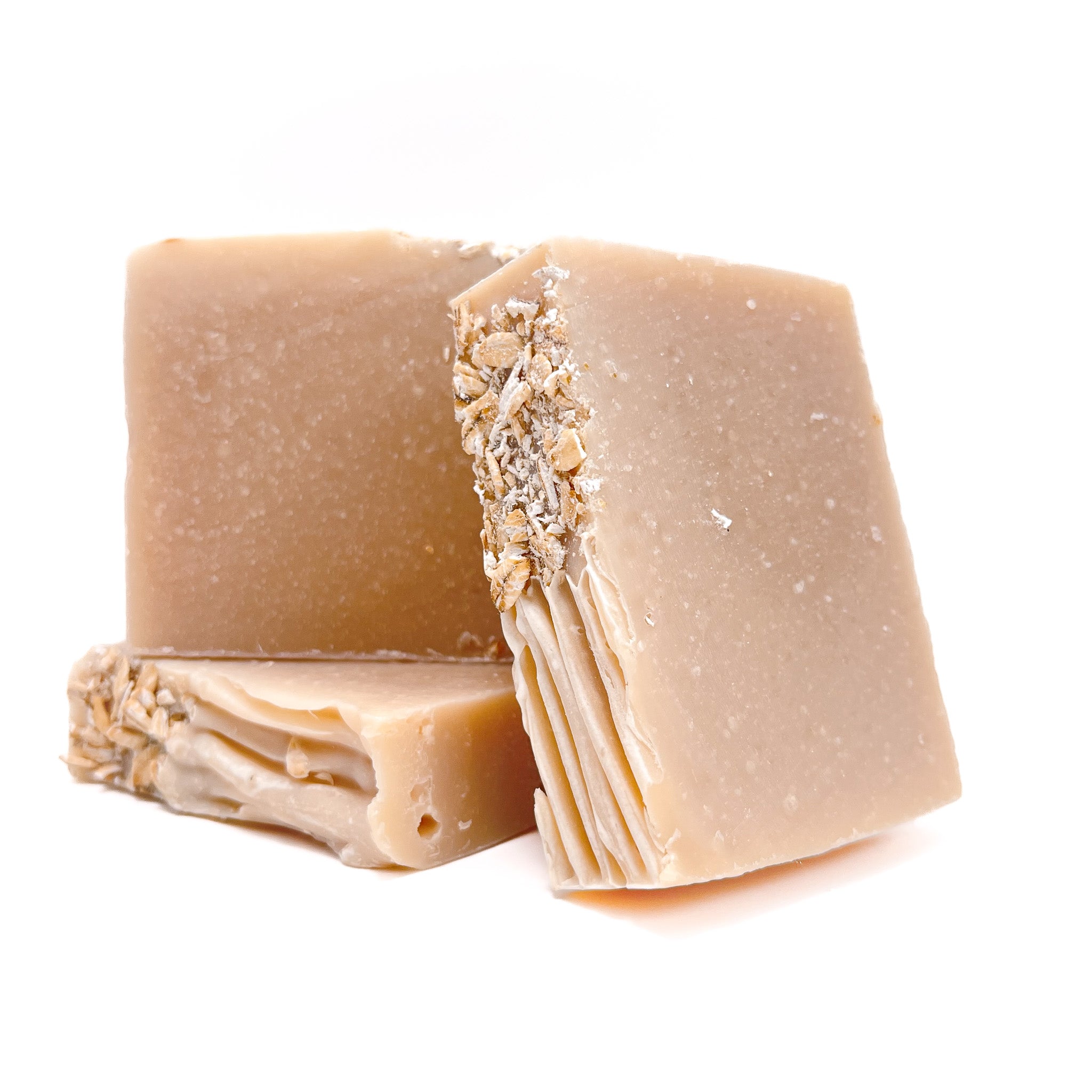 Three bars of handmade natural colored oat-milk and honey soap. Two upright and one lying flat to show texture.