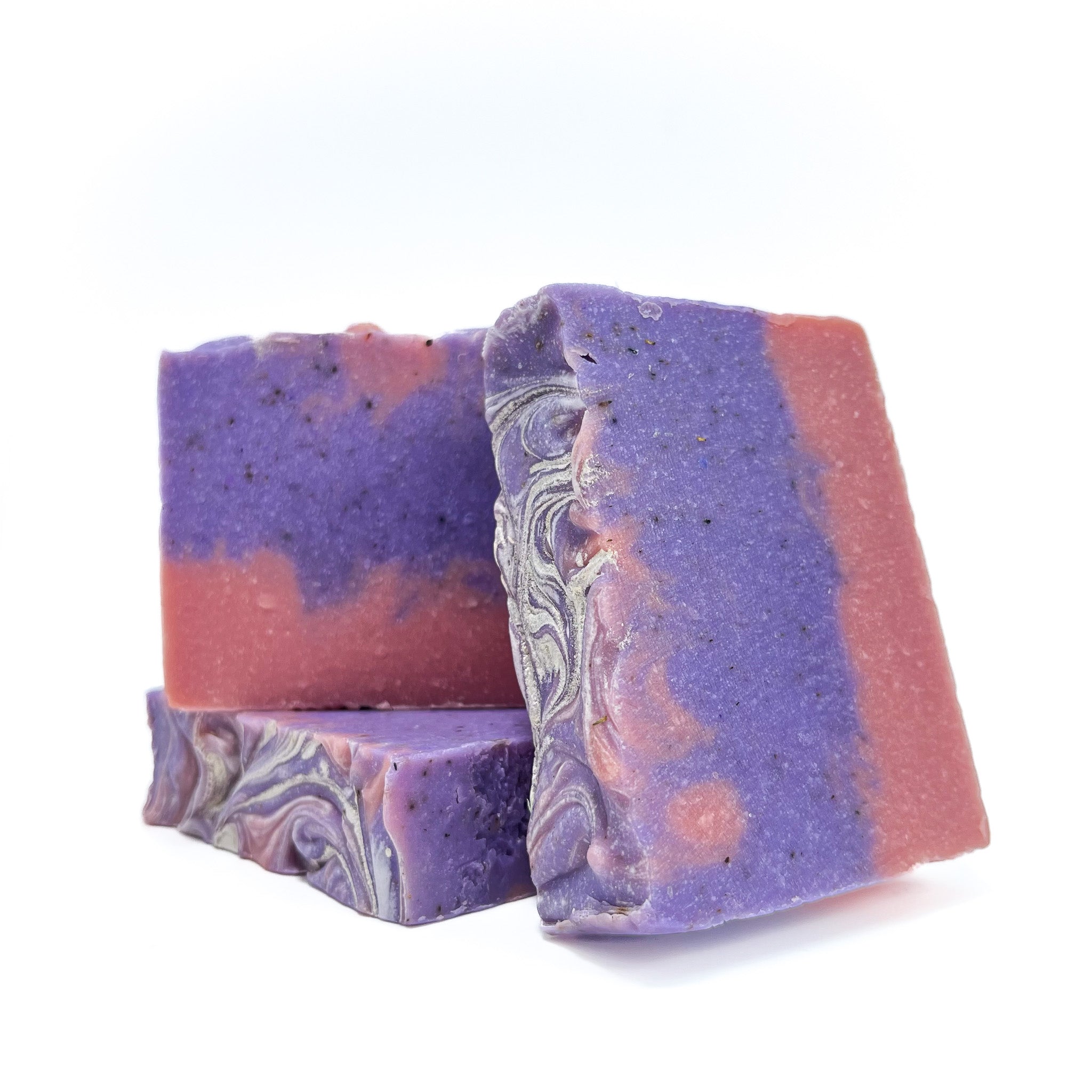 Three handmade raspberry vanilla bar soaps. Pink on the bottom, purple and pink swirled upper. Topped with shimmer. Two are top facing to show texture.