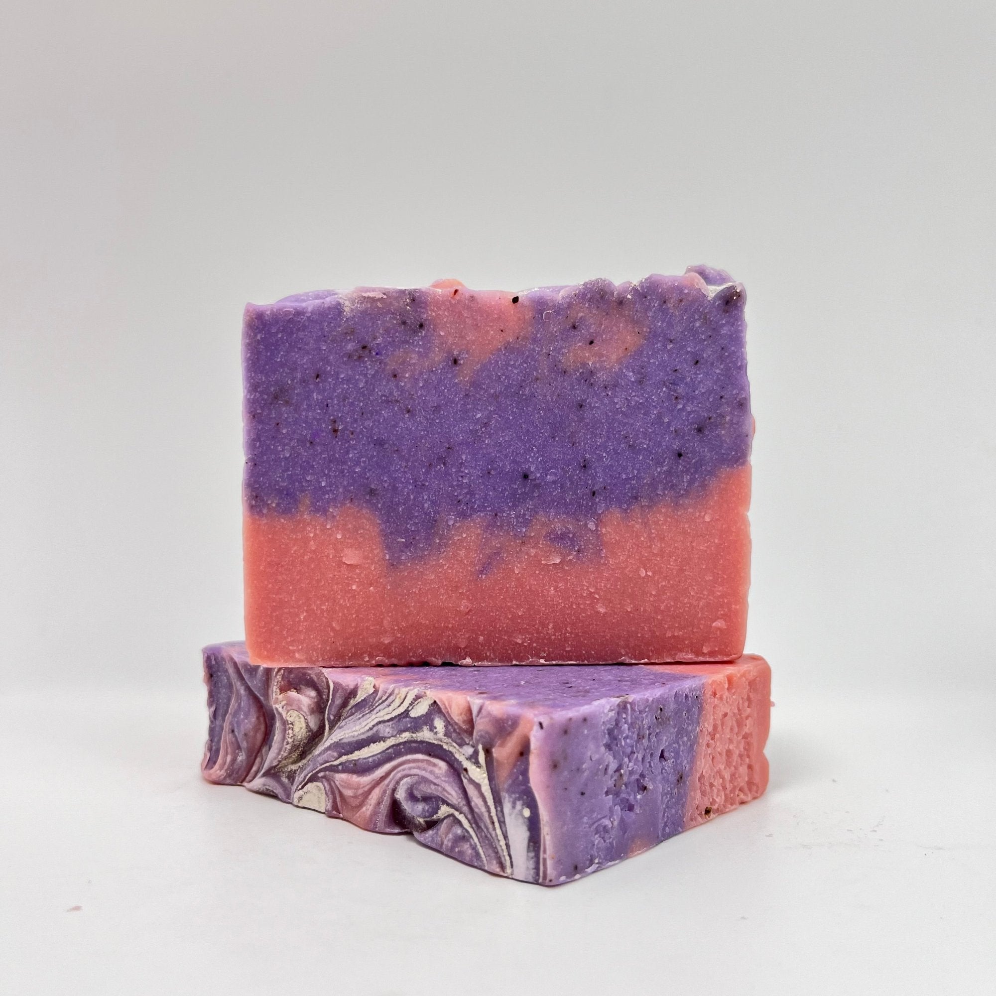 Two handmade raspberry vanilla bar soaps. Pink on the bottom, purple and pink swirled upper. Topped with shimmer. One top facing to show texture.