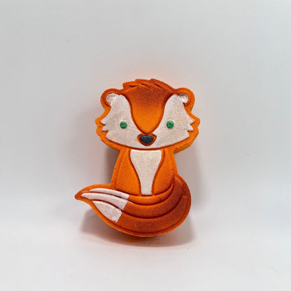 A orange fox shaped bath bomb hand-painted white face, chest, and tail tip. Green eyes, black nose, airbrush highlights.