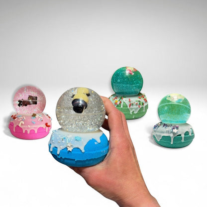 Four Snow Globe bath bombs from Rusted Acre Soap Co.. One in a hand.