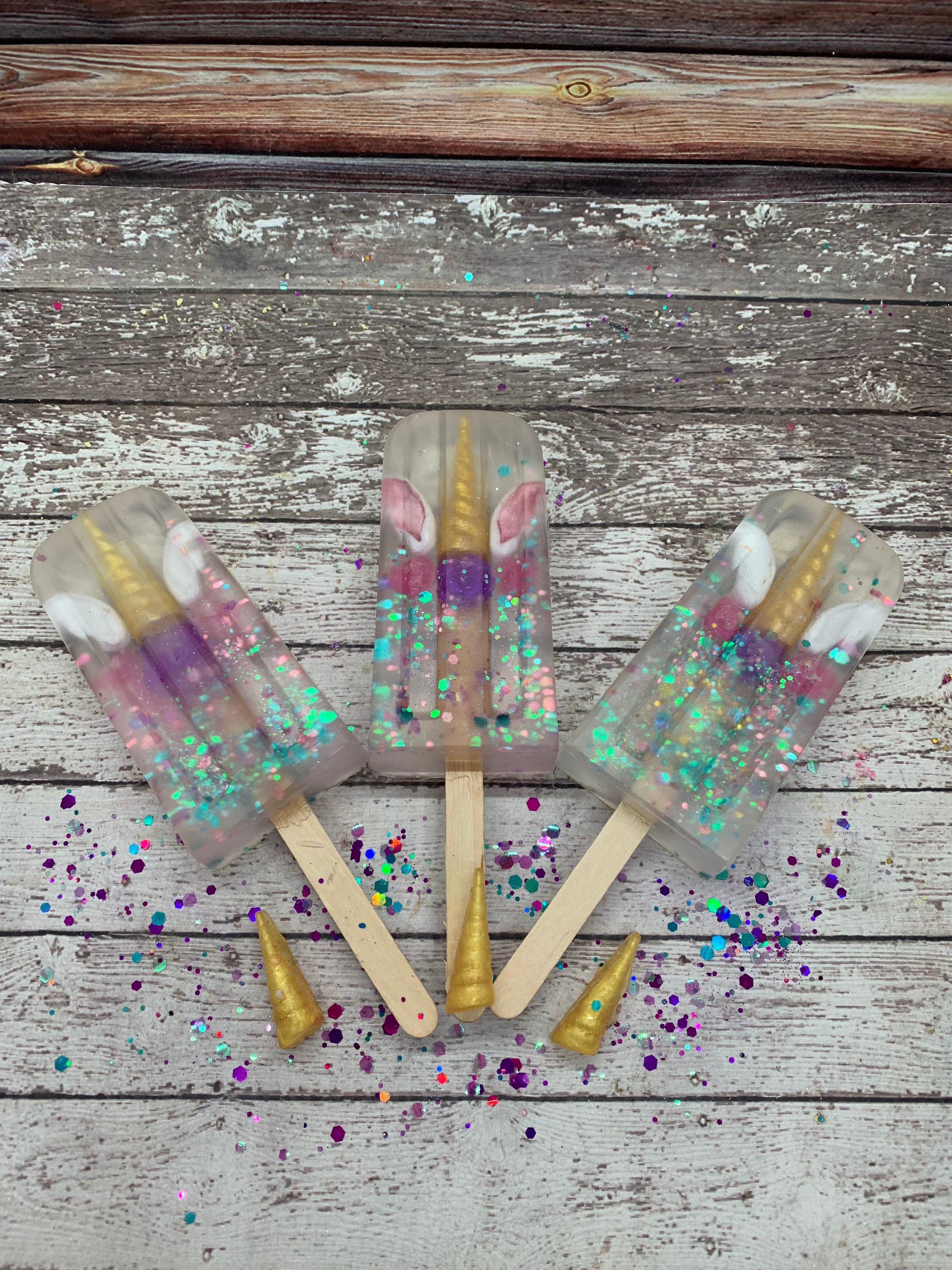 Clear soap with unicorn themed embed. Made on a popcicle stick. Purple and gold are the most abundant colors.